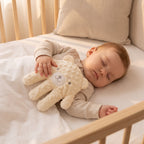 Baby Sleep Aid Patting Hand in cream bear design next to a sleeping baby in a cot