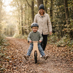 Child on a balance bike on a forest path with a parent walking behind
