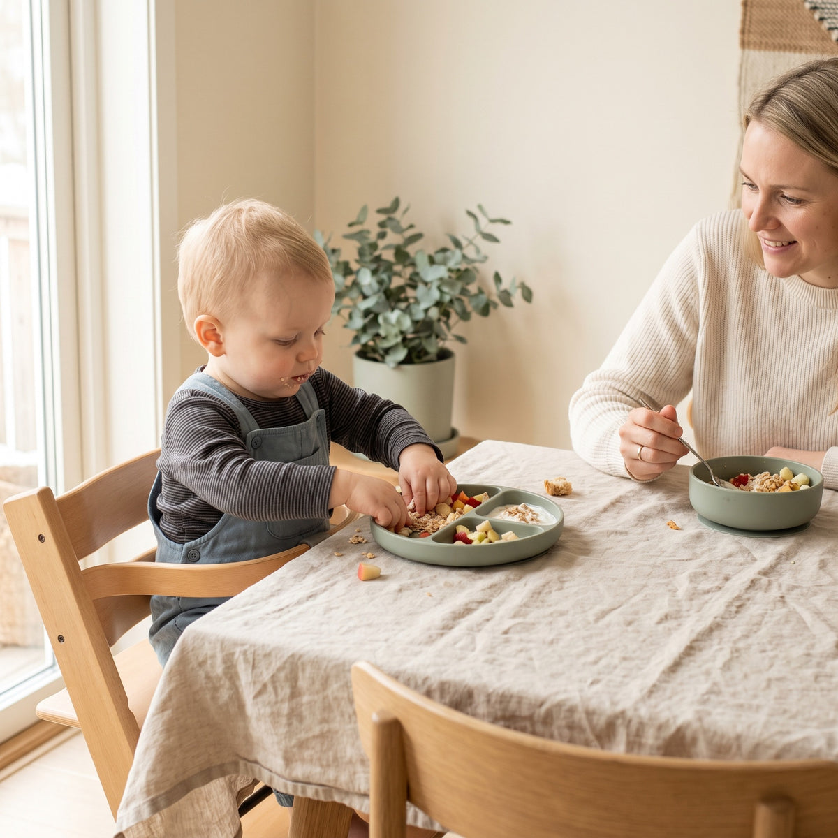 Toddler in a high chair eating from a divided plate alongside a parent